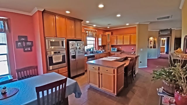 kitchen featuring sink, a center island, appliances with stainless steel finishes, dark tile patterned flooring, and ornamental molding