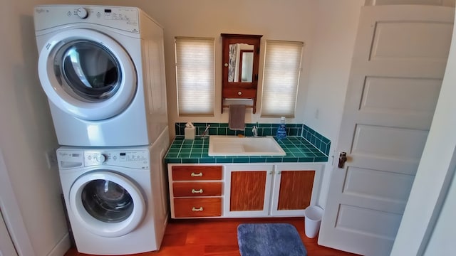 washroom with hardwood / wood-style floors, stacked washer / drying machine, and sink