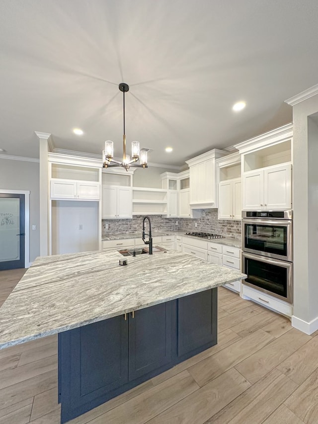 kitchen featuring white cabinetry, sink, hanging light fixtures, a large island with sink, and ornamental molding