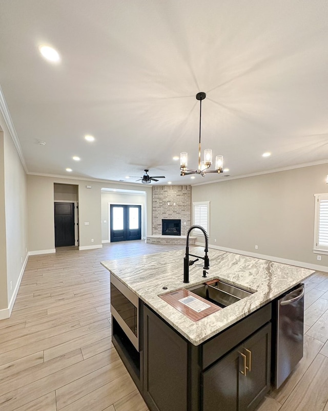 kitchen with a kitchen island with sink, ceiling fan with notable chandelier, sink, crown molding, and appliances with stainless steel finishes