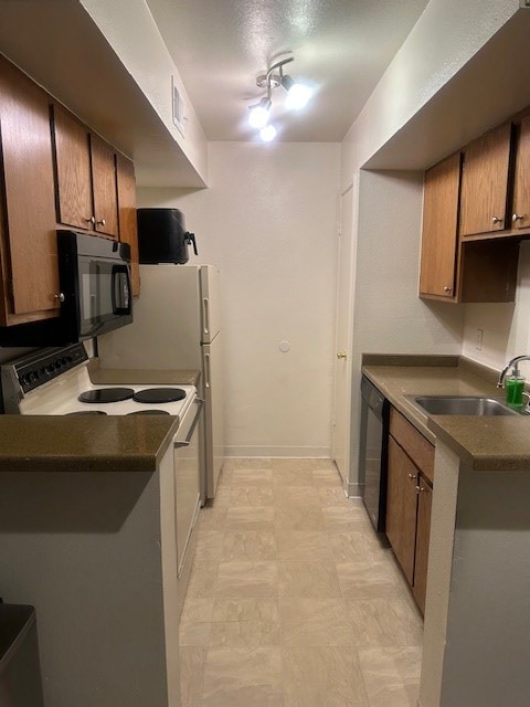 kitchen featuring brown cabinets, dark countertops, a sink, black appliances, and baseboards