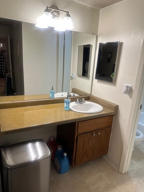 bathroom with a textured ceiling, vanity, and toilet