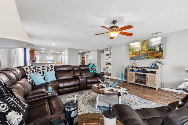 living room with wood-type flooring, a textured ceiling, ceiling fan, and built in shelves