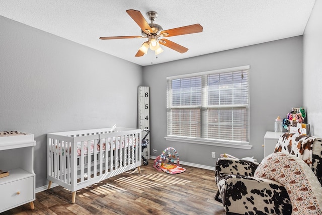 bedroom featuring hardwood / wood-style floors, ceiling fan, a textured ceiling, and a nursery area