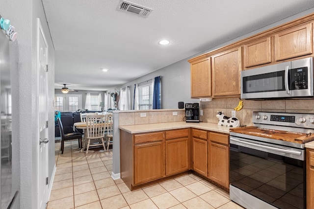 kitchen featuring kitchen peninsula, backsplash, stainless steel appliances, ceiling fan, and light tile patterned floors