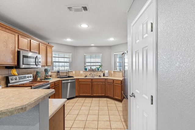 kitchen featuring appliances with stainless steel finishes, tasteful backsplash, a textured ceiling, sink, and light tile patterned floors