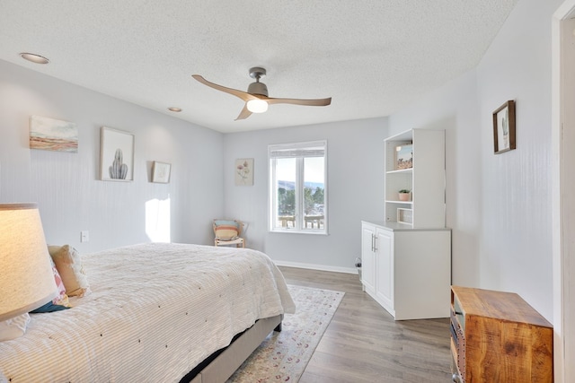 bedroom featuring ceiling fan, baseboards, a textured ceiling, and wood finished floors