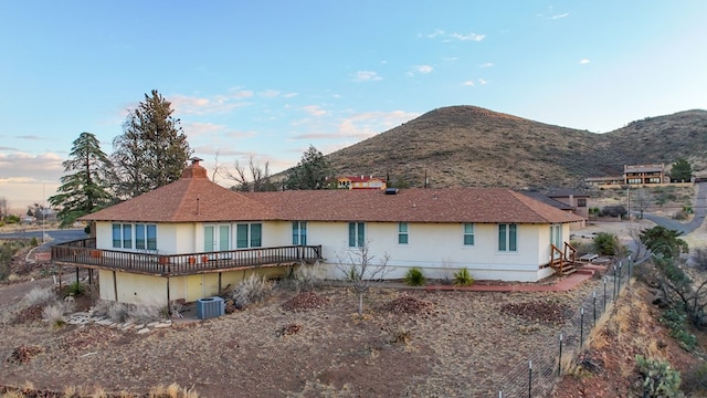 rear view of property with cooling unit, a chimney, a mountain view, and stucco siding