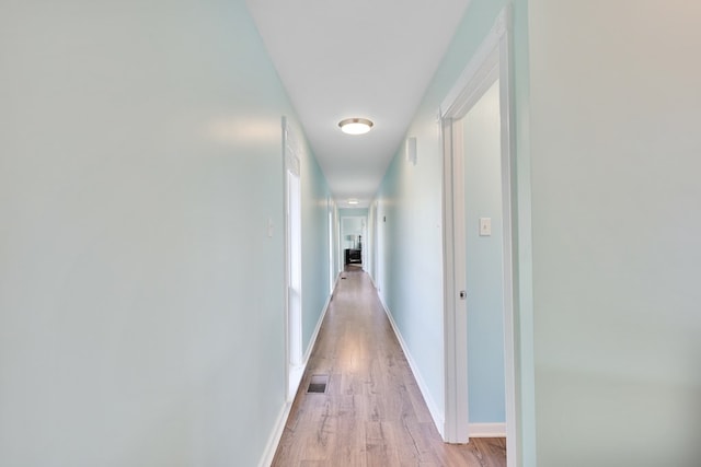 corridor featuring visible vents, baseboards, and light wood finished floors