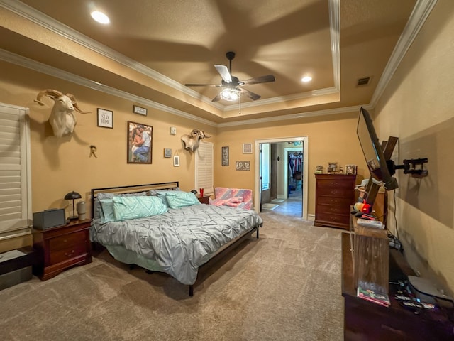 bedroom featuring ceiling fan, carpet, ornamental molding, a walk in closet, and a raised ceiling