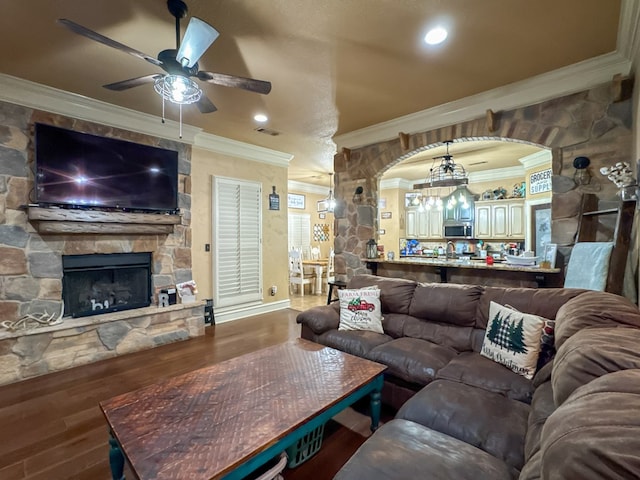 living room featuring crown molding, ceiling fan, wood-type flooring, and a stone fireplace