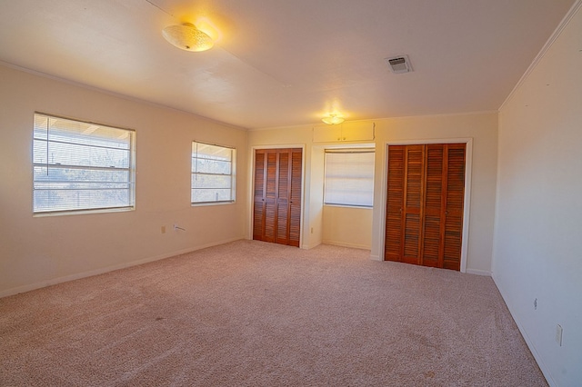 unfurnished bedroom featuring carpet, two closets, and ornamental molding