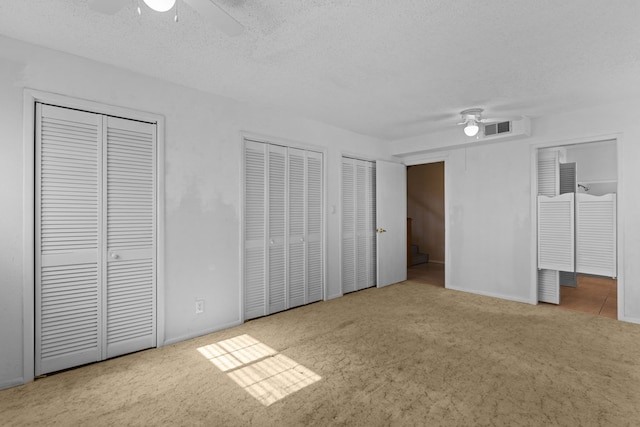 unfurnished bedroom with multiple closets, ceiling fan, light colored carpet, and a textured ceiling