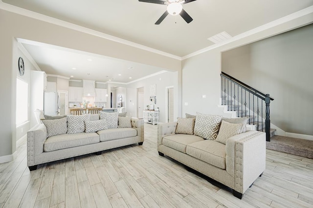 living room with ceiling fan, light wood-style flooring, baseboards, stairs, and crown molding