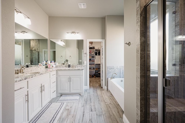 bathroom featuring double vanity, wood finished floors, a garden tub, a spacious closet, and a shower stall