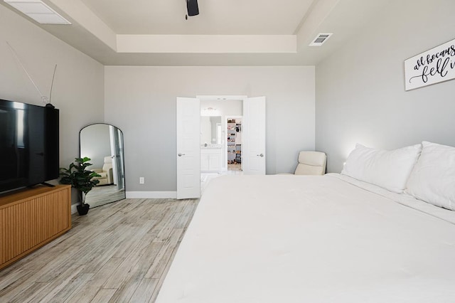 bedroom featuring light wood-type flooring, a raised ceiling, visible vents, and baseboards