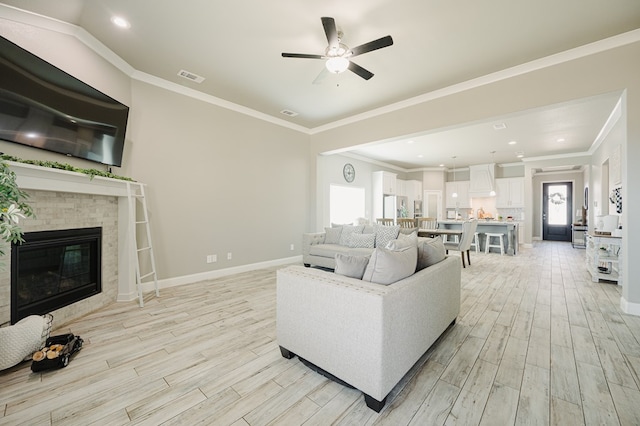 living room with crown molding, visible vents, a brick fireplace, light wood-type flooring, and baseboards