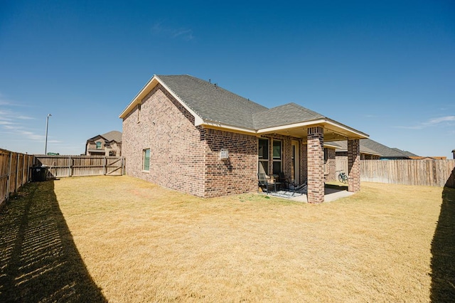 back of house with a shingled roof, a fenced backyard, a yard, a patio area, and brick siding