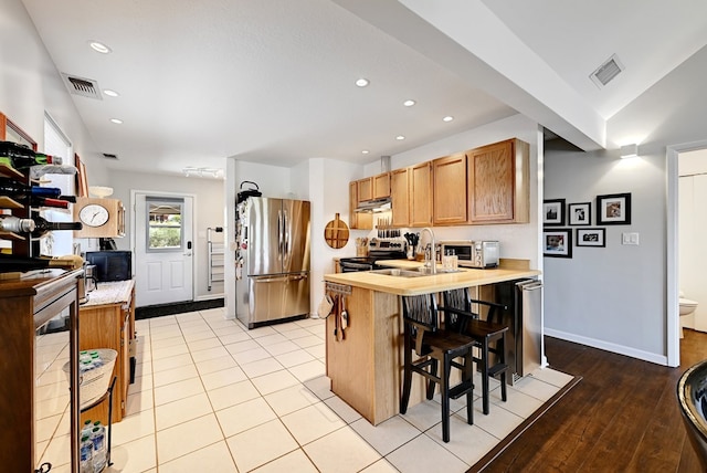 kitchen with sink, stainless steel appliances, an island with sink, a kitchen bar, and light wood-type flooring