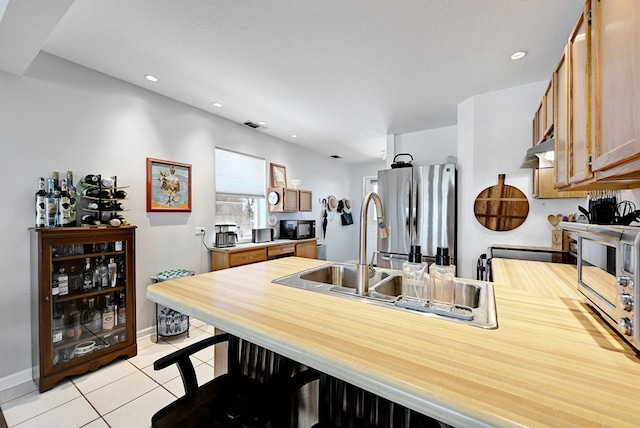 kitchen with a textured ceiling, light tile patterned flooring, sink, and stainless steel refrigerator