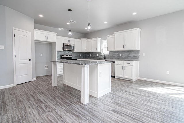 kitchen with stainless steel appliances, white cabinetry, light stone countertops, and a center island