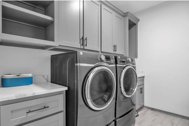 clothes washing area featuring washing machine and dryer, cabinet space, and light wood finished floors