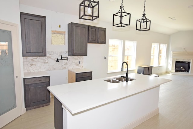 kitchen featuring pendant lighting, sink, light wood-type flooring, an island with sink, and dark brown cabinets