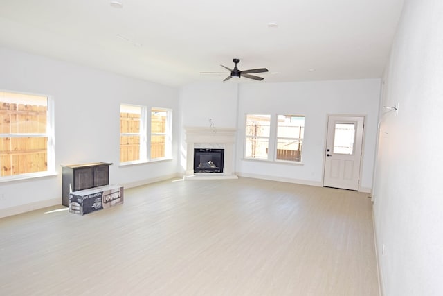 unfurnished living room with a high end fireplace, light hardwood / wood-style floors, ceiling fan, and a healthy amount of sunlight