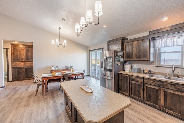 kitchen featuring decorative light fixtures, lofted ceiling, sink, stainless steel fridge, and a center island