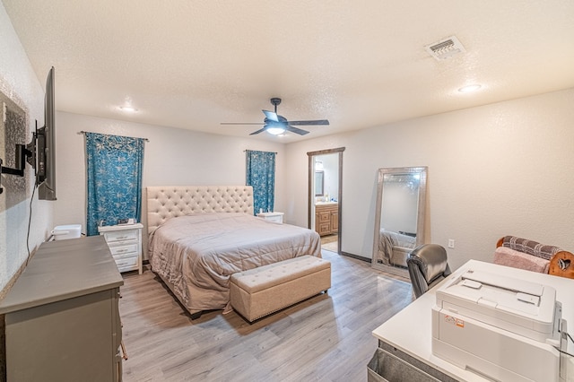 bedroom featuring ceiling fan, ensuite bathroom, light hardwood / wood-style floors, and a textured ceiling