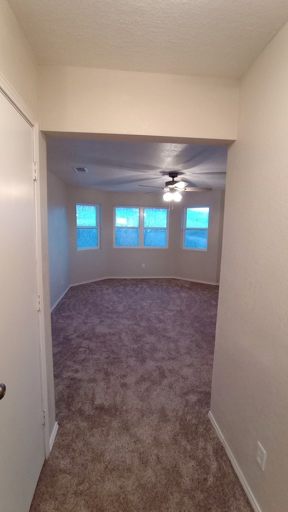 unfurnished room featuring dark colored carpet, a textured ceiling, ceiling fan, and a healthy amount of sunlight