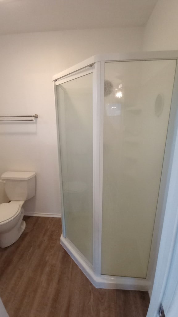 bathroom featuring wood-type flooring, a shower with shower door, and toilet