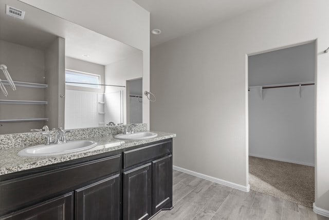 bathroom with double vanity, visible vents, a walk in closet, and a sink