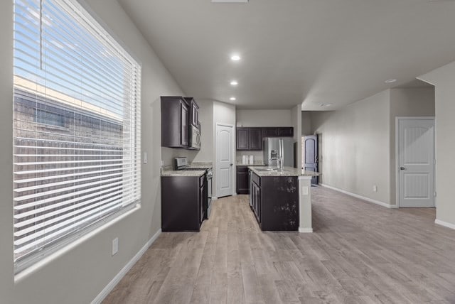 kitchen featuring a center island with sink, recessed lighting, light wood-style floors, appliances with stainless steel finishes, and baseboards