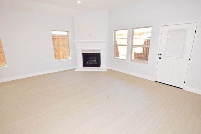 unfurnished living room with lofted ceiling, a high end fireplace, and light wood-type flooring