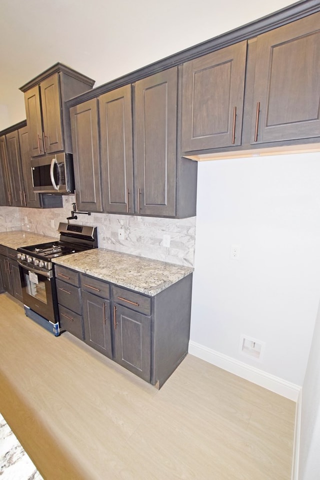 kitchen with stainless steel appliances, light stone countertops, dark brown cabinets, and backsplash