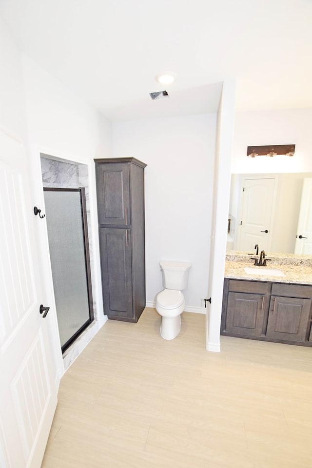 bathroom featuring vanity, wood-type flooring, a shower with shower door, and toilet