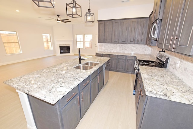 kitchen featuring pendant lighting, sink, light stone counters, stainless steel appliances, and a center island with sink