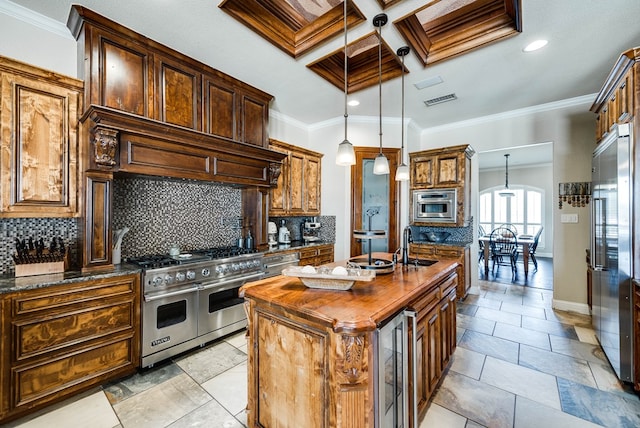 kitchen with high end appliances, coffered ceiling, a center island with sink, ornamental molding, and decorative light fixtures