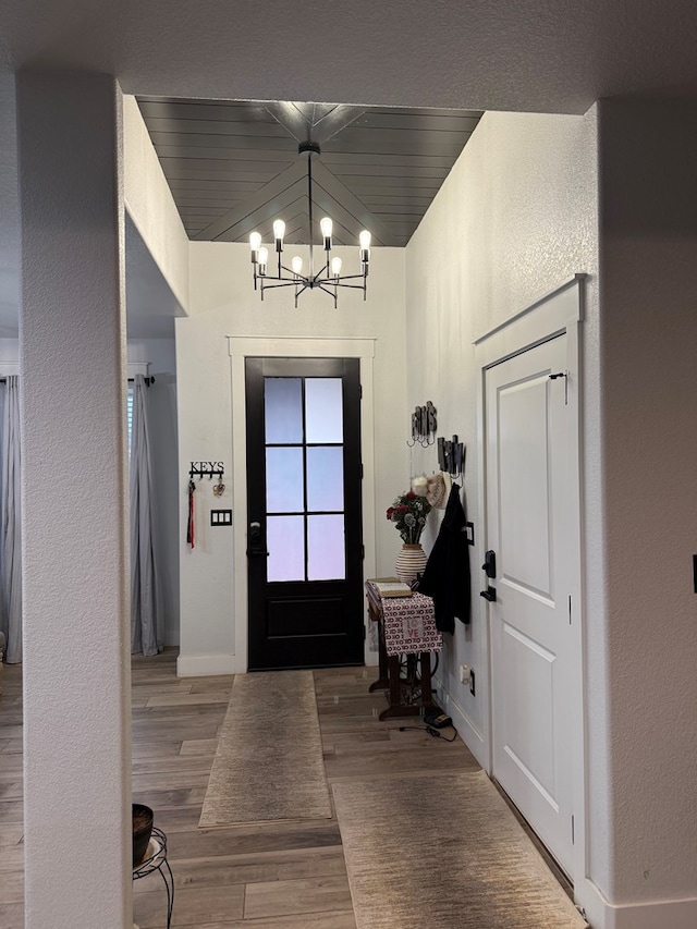 foyer entrance featuring an inviting chandelier, baseboards, wood finished floors, and a textured wall