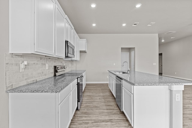 kitchen featuring sink, an island with sink, appliances with stainless steel finishes, light stone counters, and white cabinetry