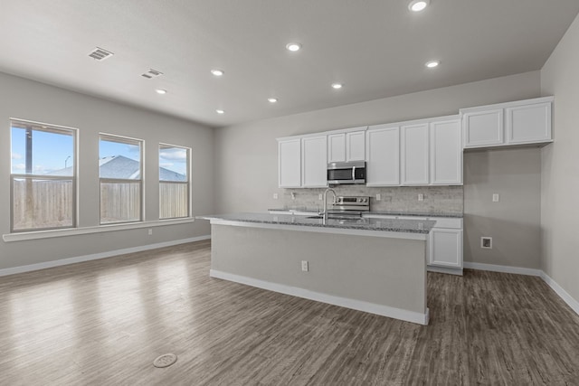 kitchen with light stone countertops, stainless steel appliances, a kitchen island with sink, dark wood-type flooring, and white cabinets