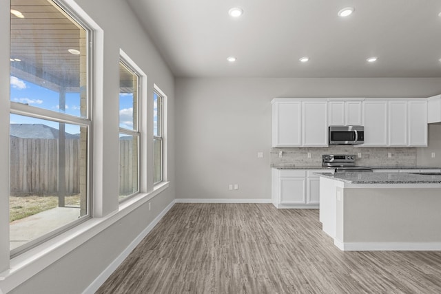 kitchen with decorative backsplash, appliances with stainless steel finishes, light stone counters, light hardwood / wood-style flooring, and white cabinetry