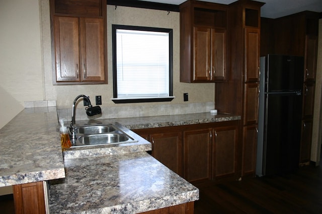 kitchen with kitchen peninsula, dark hardwood / wood-style flooring, black fridge, and sink