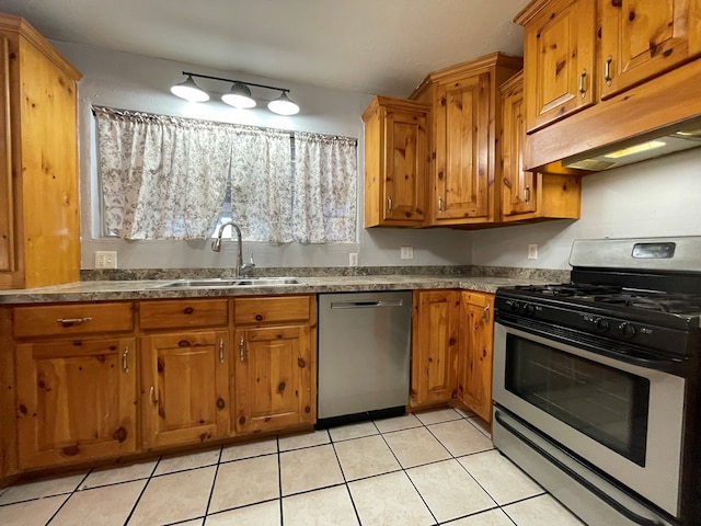 kitchen with brown cabinetry, stainless steel appliances, under cabinet range hood, a sink, and light tile patterned flooring