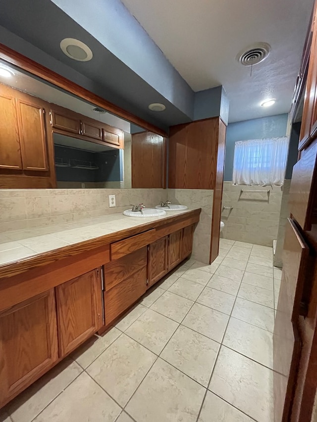 bathroom with a wainscoted wall, tile walls, visible vents, vanity, and tile patterned flooring