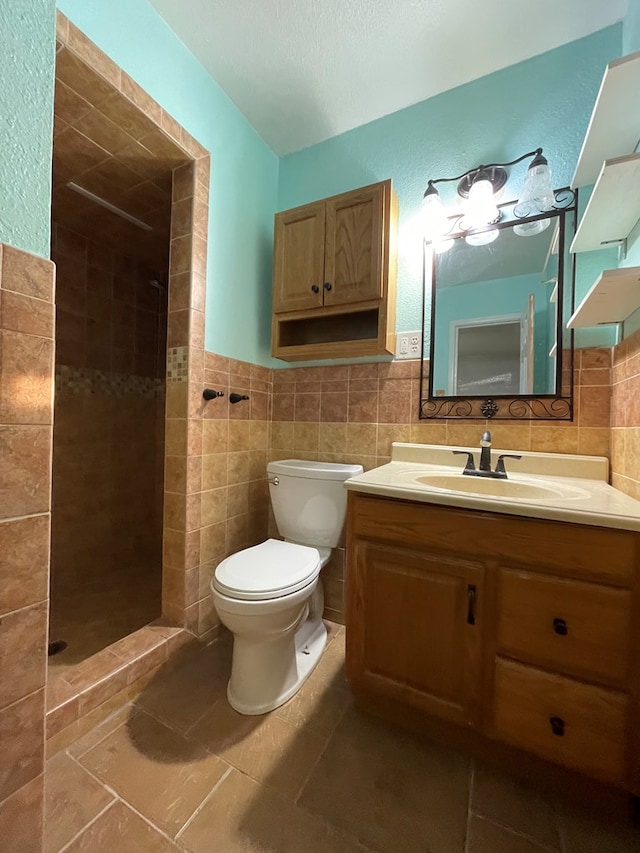 bathroom featuring toilet, vanity, tile walls, tiled shower, and tile patterned floors