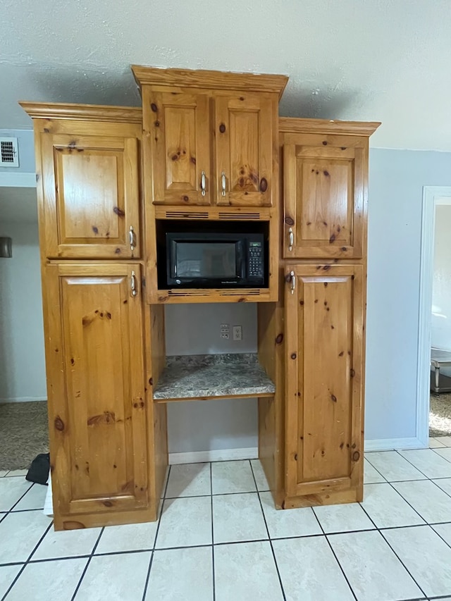 interior space featuring brown cabinets, visible vents, light tile patterned flooring, black microwave, and baseboards