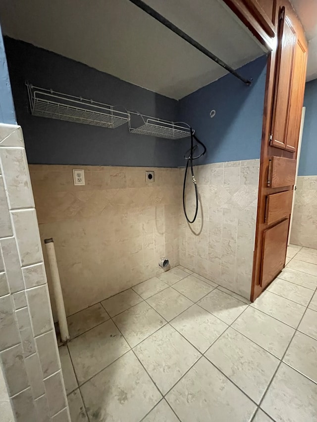 interior space with light tile patterned floors, wainscoting, electric dryer hookup, and tile walls