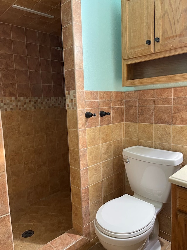 bathroom with a wainscoted wall, tile walls, toilet, a tile shower, and vanity